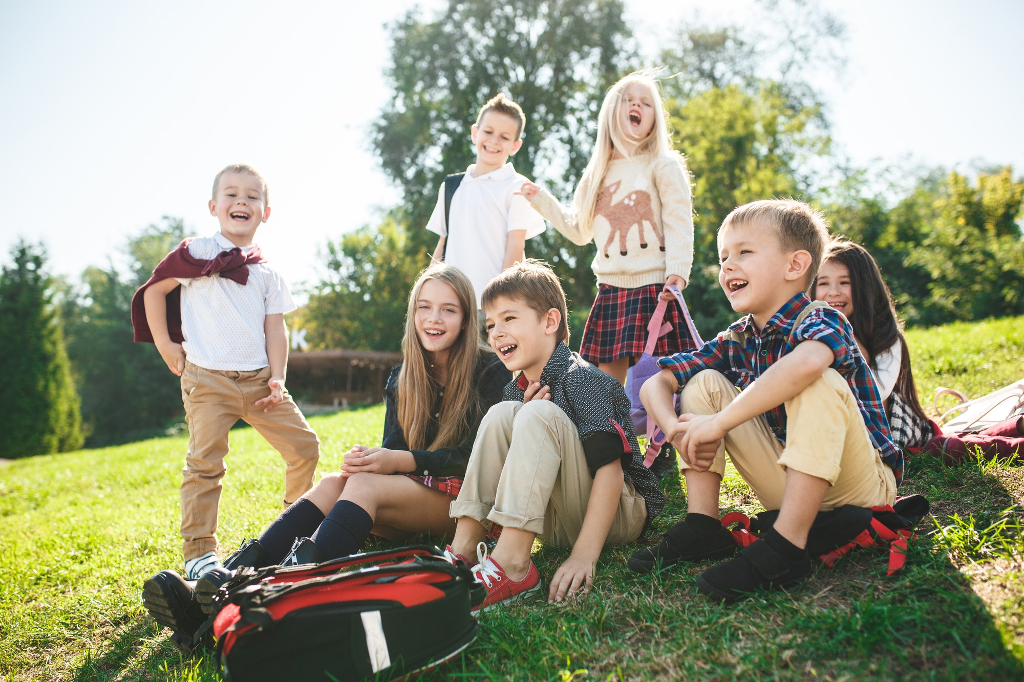 A group of children of school and preschool age are sitting on the green grass in the park.