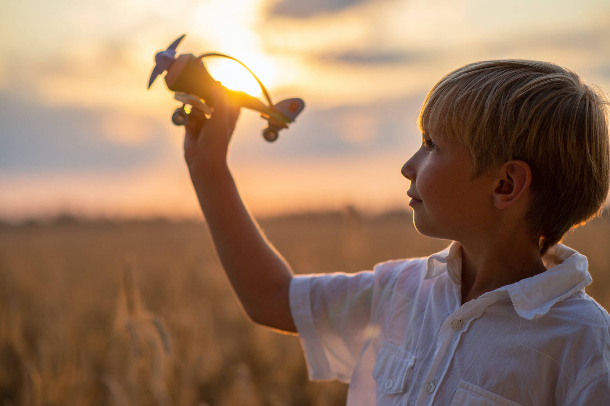 Boy in a white shirt with a plane in hands against sky. Kid hol
