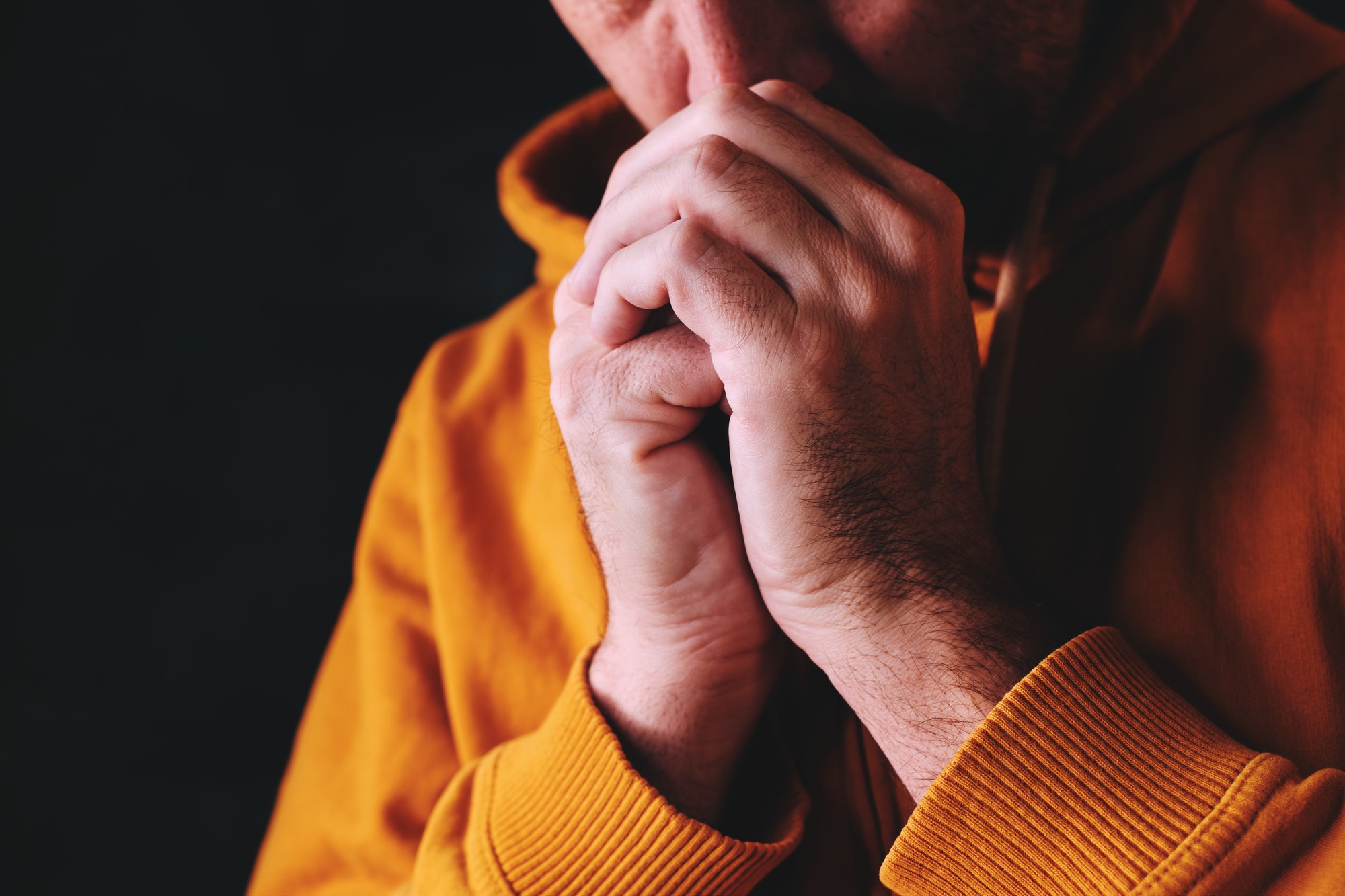 Christian man praying to God in dark room with clasped hands